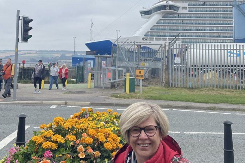 Et fodgængerfelt med lyssignaler, en blomsterbed med gule blomster og et krydstogtskib i baggrunden. 2