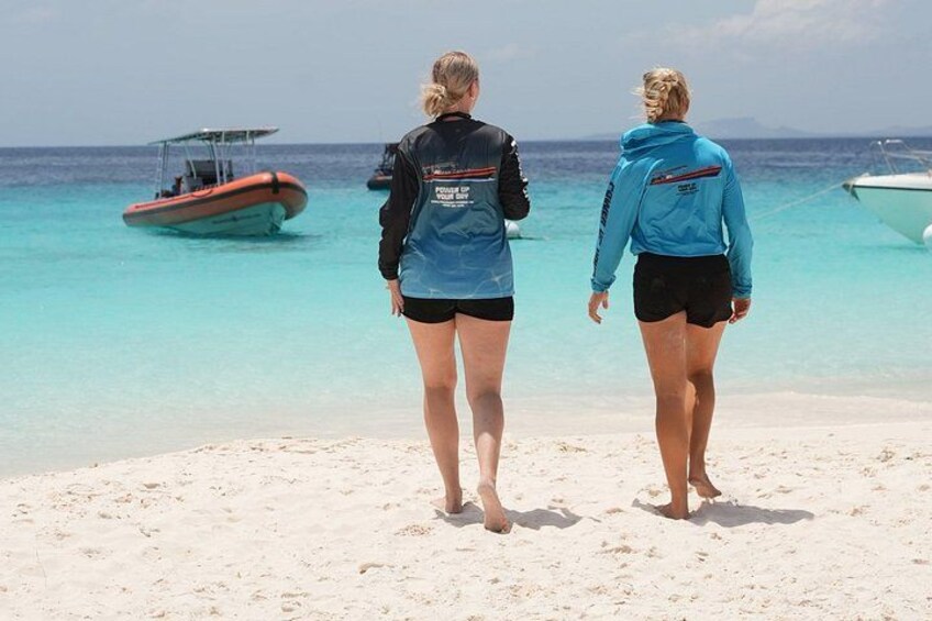 Two people walking on a beach with a boat in the water. 2