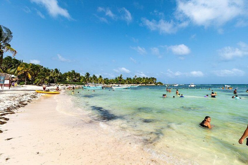 A beach with clear turquoise water, people swimming and sunbathing, and palm trees lining the shore. 3