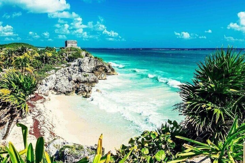 A coastal landscape with a beach, ocean waves, and a small structure on a rocky outcrop. 1