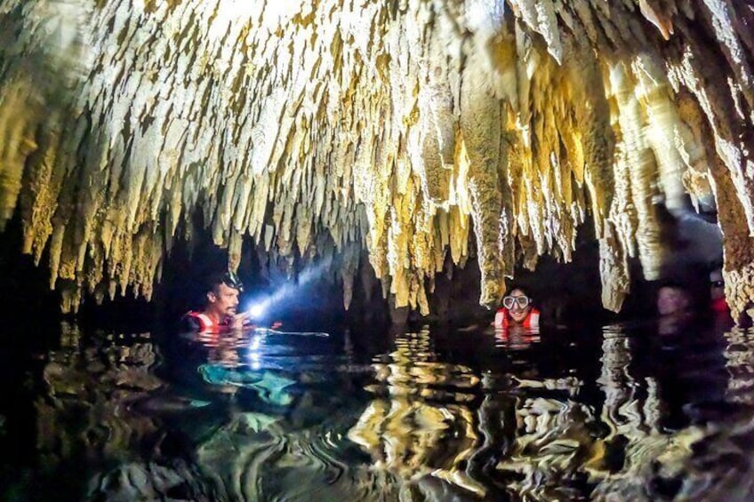 A cave with stalactites and stalagmites, and two people exploring the interior. 5