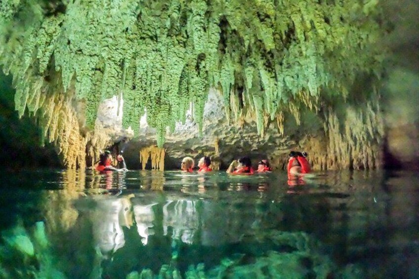A cave with stalactites and stalagmites, water, and people in red life jackets. 5