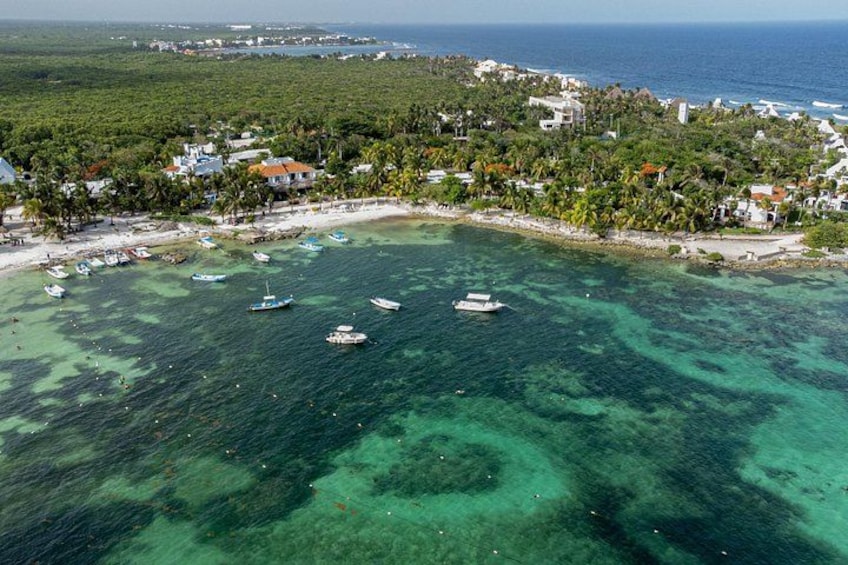 An aerial view of a coastal area with clear turquoise waters, boats, and a dense cluster of buildings surrounded by greenery. 5