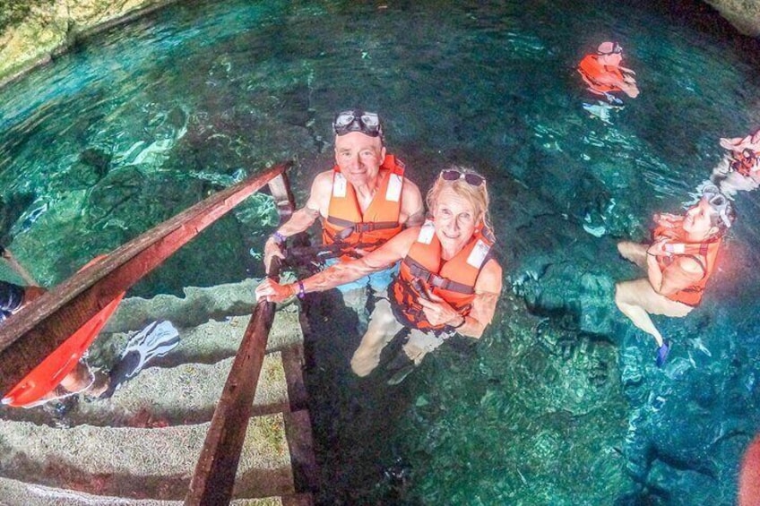 People in clear water, wearing life jackets, and using a wooden ladder to climb out. 3