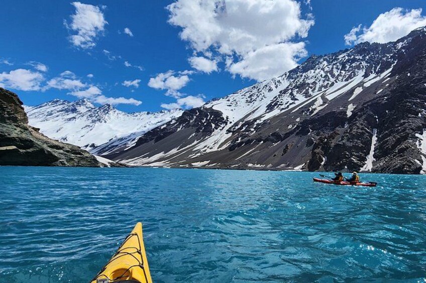 A kayaker in a yellow kayak on a clear blue lake with snow-capped mountains in the background. 3