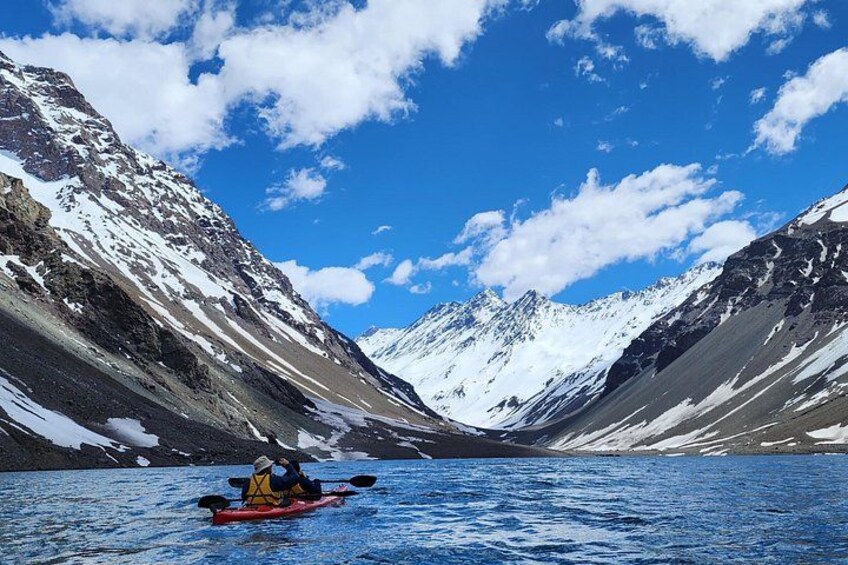 A kayaker on a red kayak in a calm body of water surrounded by snow-covered mountains under a clear blue sky. 4