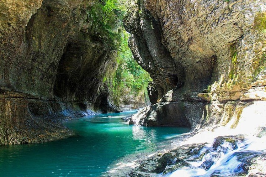 Une rivière turquoise serpente à travers un canyon rocheux, bordée d’une végétation luxuriante. 3