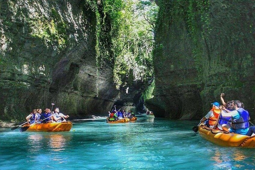 People rafting on a river surrounded by rocky cliffs and greenery. 1