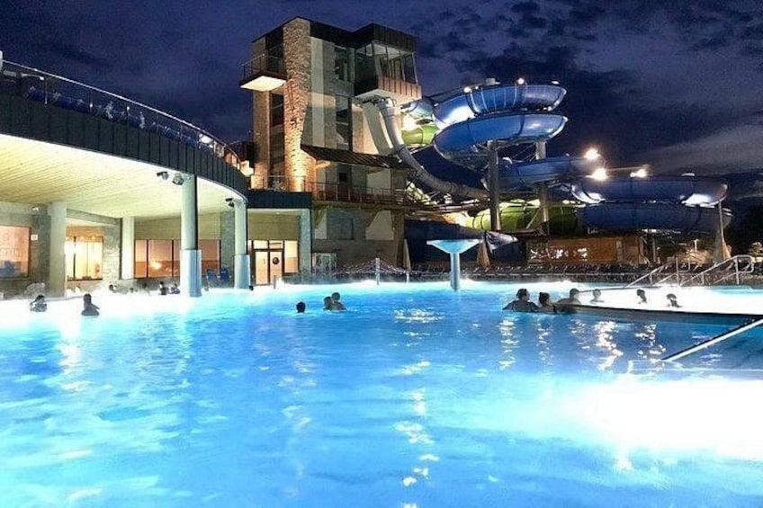 Una piscina con gente, un tobogán acuático y un edificio de diseño singular. 5