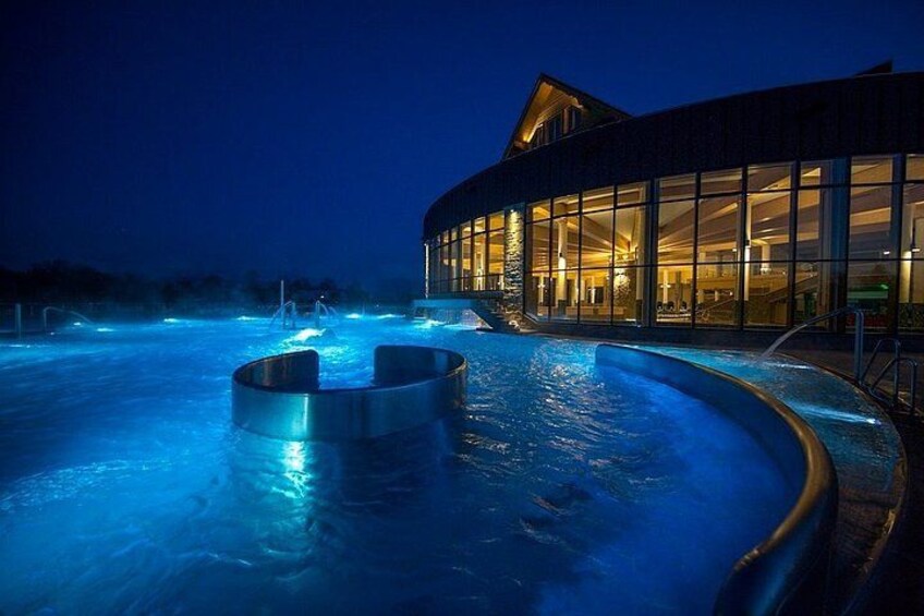 Piscina al aire libre climatizada de noche, con un edificio al fondo. 2