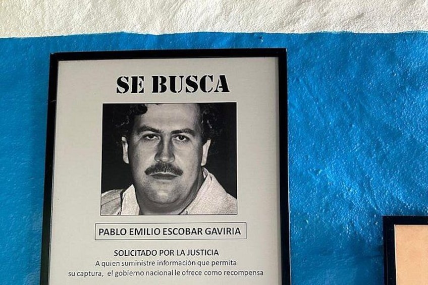 A framed poster with a man's face, the text 'SE BUSCA' and 'PABLO EMILIO ESCOBAR GAVIRIA' on it. 2