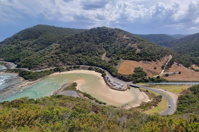 Eine Küstenlandschaft mit einer kurvenreichen Straße, einem Strand und bewaldeten Hügeln. 3