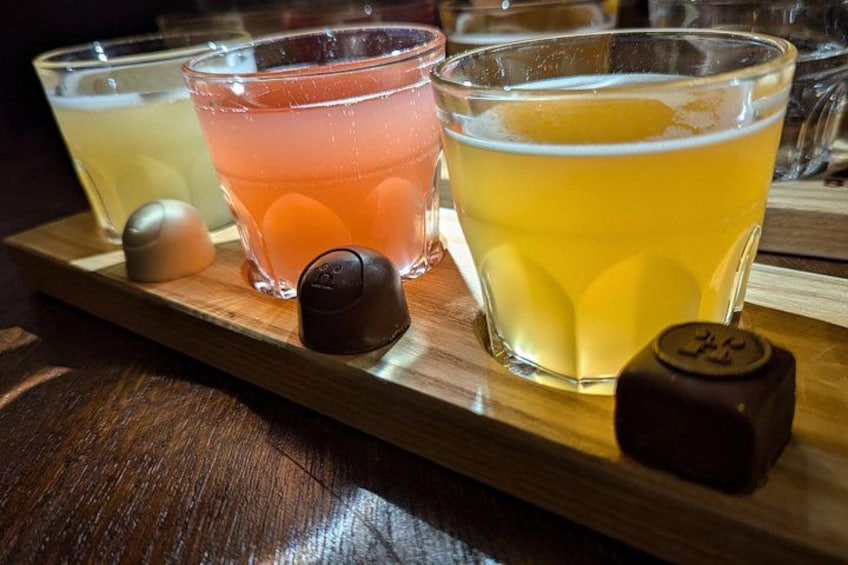 A wooden tray with three glasses of different colored beverages and two chocolate-covered items. 2