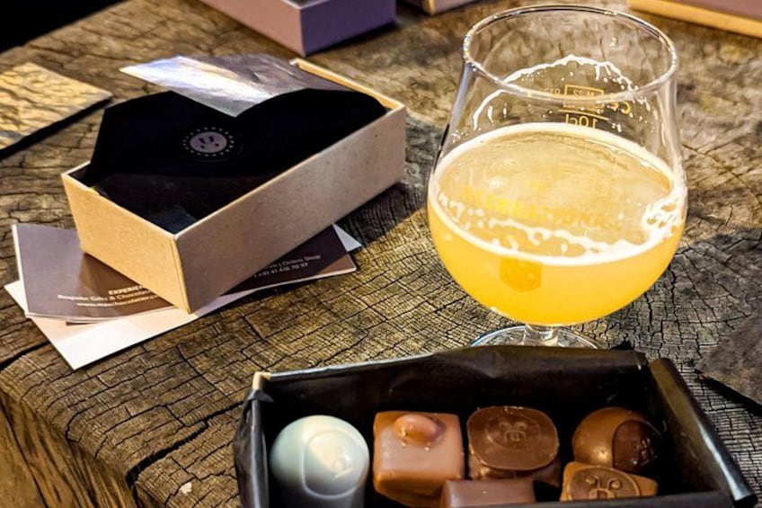 A wooden table with a glass of beer, a box of chocolates, and business cards. 5