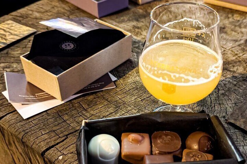 A wooden table with a glass of beer, a box of chocolates, and some cards. 1