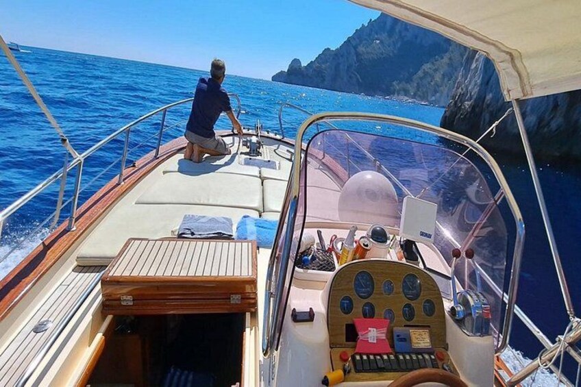 Un bateau avec une personne aux commandes, un pont en bois et des falaises rocheuses en arrière-plan. 2