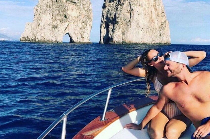 Un bateau avec deux personnes à bord, des falaises rocheuses en arrière-plan et une eau bleue et calme. 4