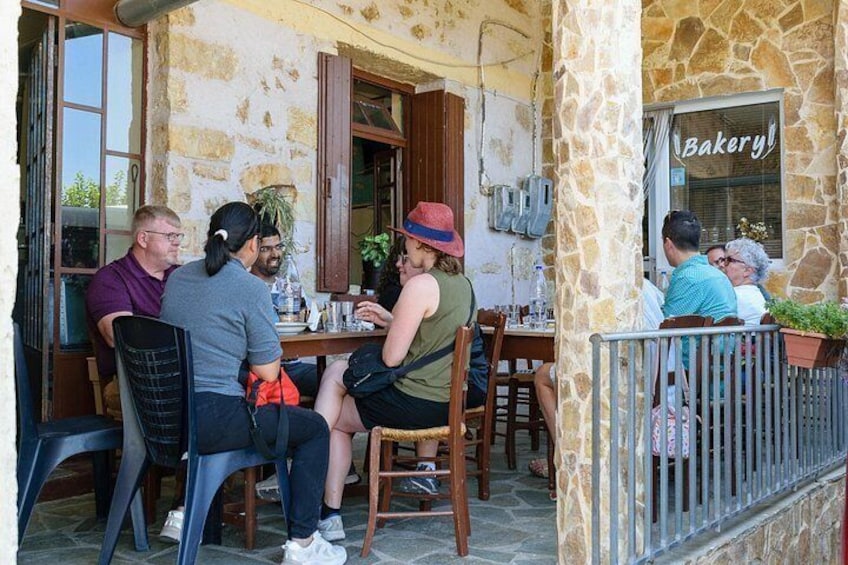 Folk spiser på en udendørs café med stenvægge og et skilt, der står 'Bakery'. 5