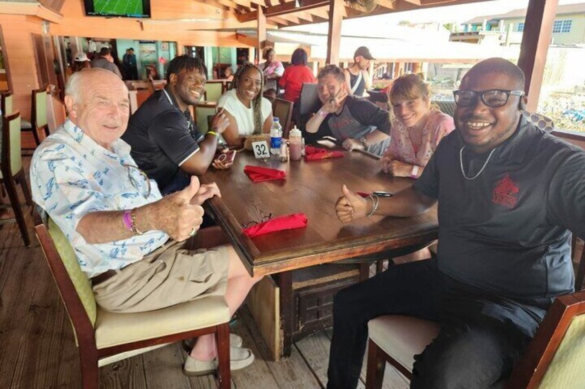 A group of people sitting around a wooden table in a restaurant with a view of the outdoors. 1