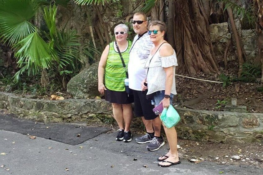 Trois personnes se tiennent sur un chemin pavé, avec de la verdure et un mur de pierre en arrière-plan. 3