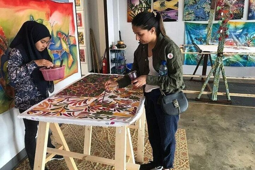 Twee personen werken aan een groot, kleurrijk schilderij op een houten schilderstatief in een kunststudio. 5