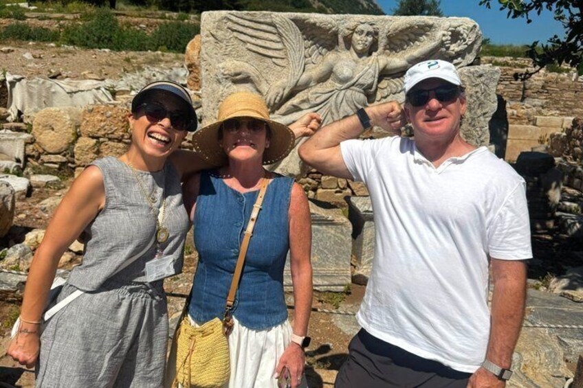 Three people standing in front of ancient ruins with stone sculptures. 2