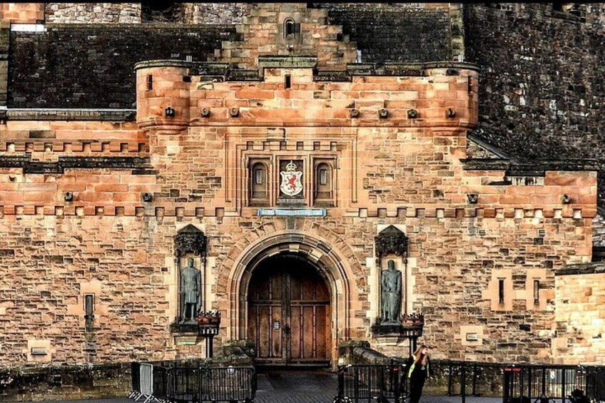 A historic stone building with a large wooden door, arched windows, and a coat of arms above the door. 2