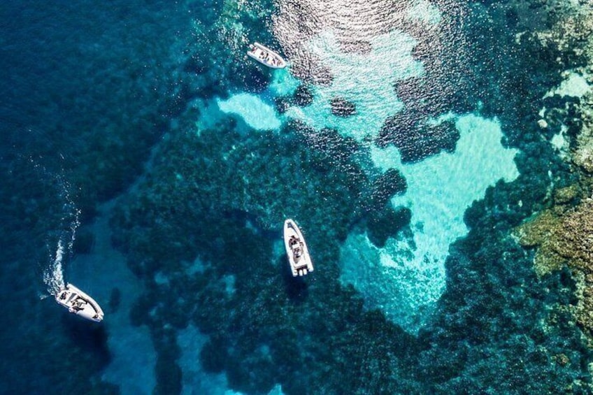 A clear blue sea with boats and a rocky underwater landscape. 2