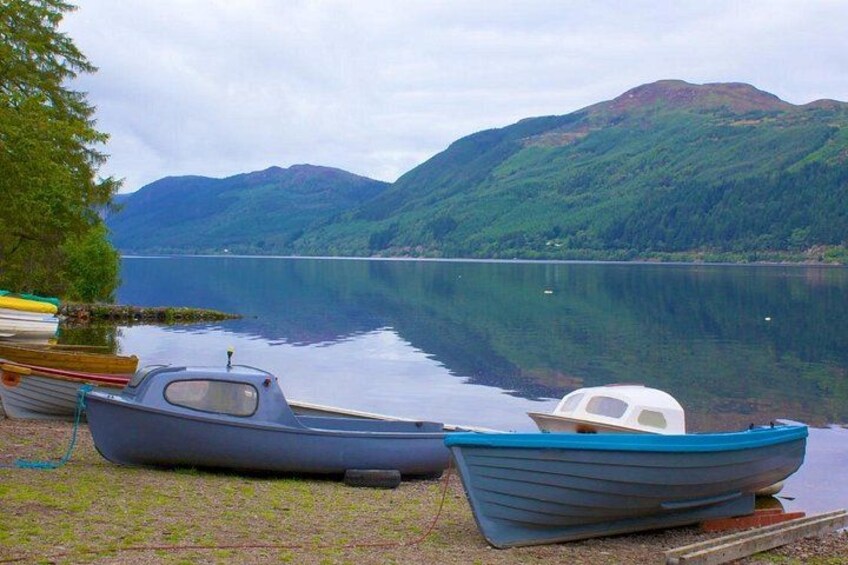 A calm lake with boats docked on the shore, surrounded by lush green hills. 2