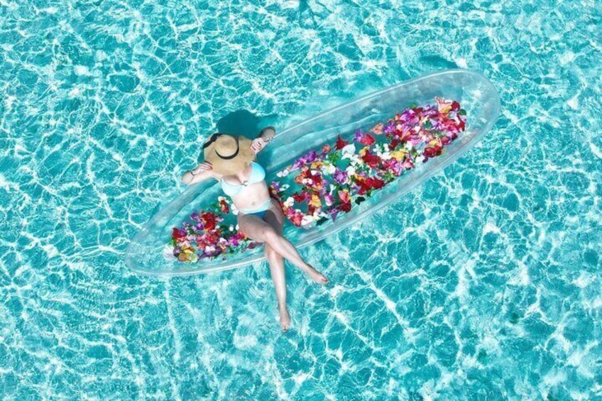 Une personne flotte sur un radeau gonflable transparent, rempli de fleurs aux couleurs vives, dans une piscine. 2