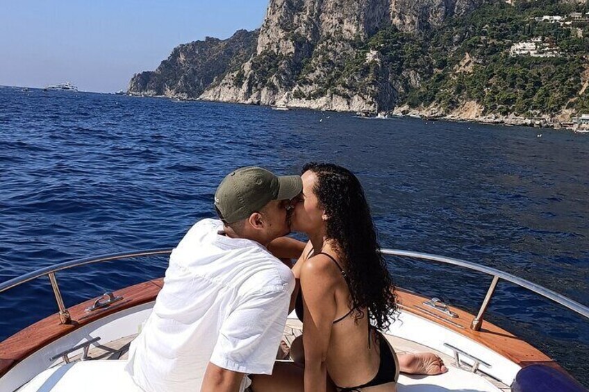 A couple kissing on a boat with a rocky coastline in the background. 5