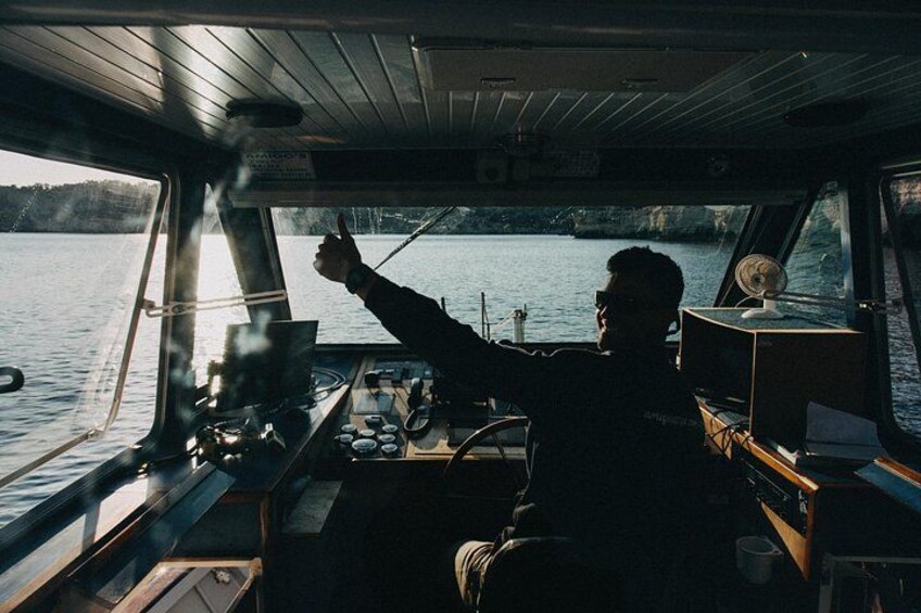 A person steering a boat, with water and a forested shoreline in the background. 2