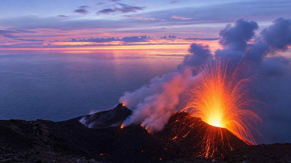 Ett vulkanutbrott vid solnedgång, med lava som rinner ner i havet. 5