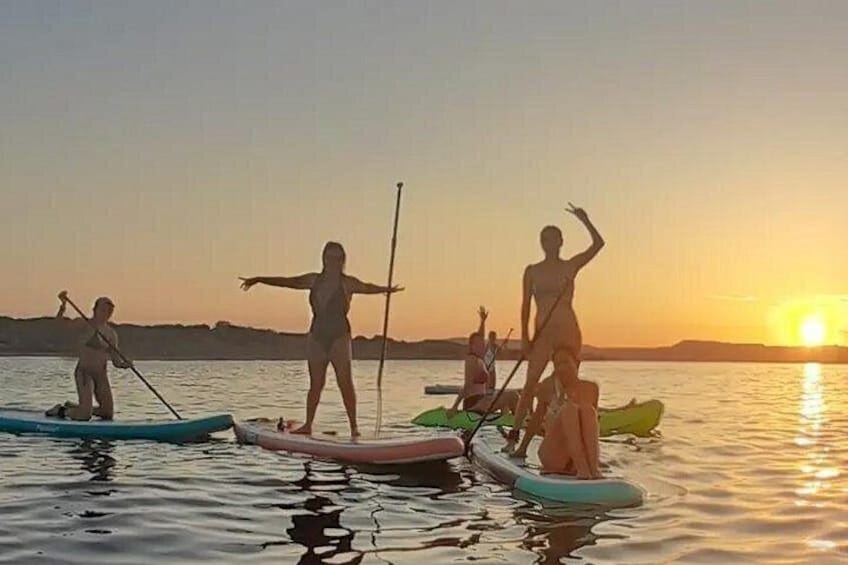Mensen staan op paddleboards op kalm water tijdens de zonsondergang. 1