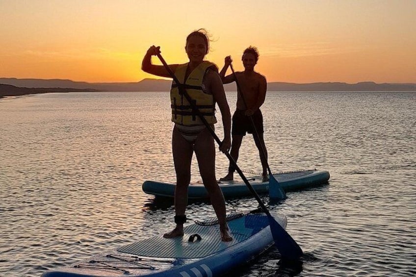 Twee mensen staan op paddleboards op een rustig wateroppervlak tijdens de zonsondergang. 5
