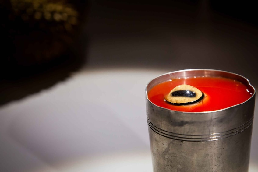 A metallic cup filled with a red liquid and a black object resembling an eye. 2