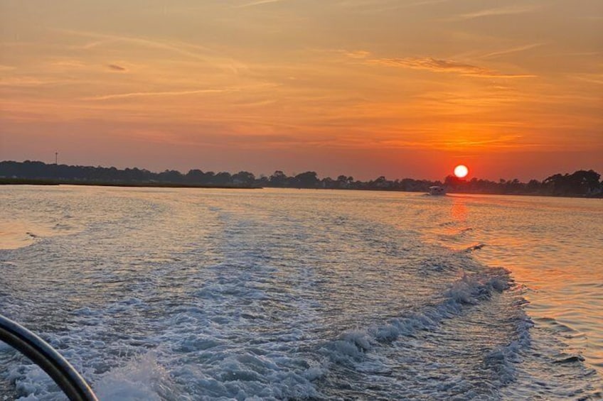 A sunset over a body of water with a boat creating a wake. 5