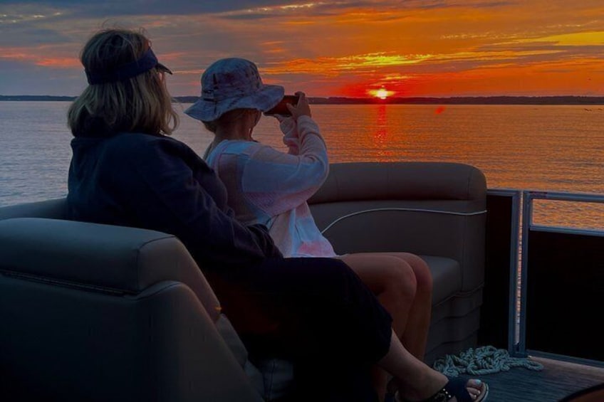 Two people on a boat watching a sunset over the water. 3