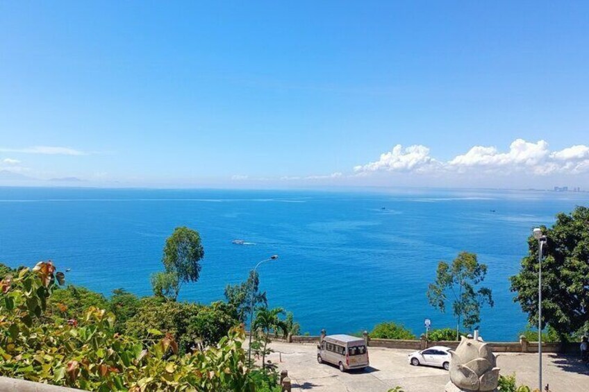 A coastal view with a clear blue sea, a parked bus, and a car on the roadside. 3