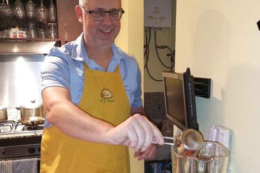 Una persona con un delantal amarillo cocina en una cocina con estufa, tazas medidoras y una balanza digital. 2
