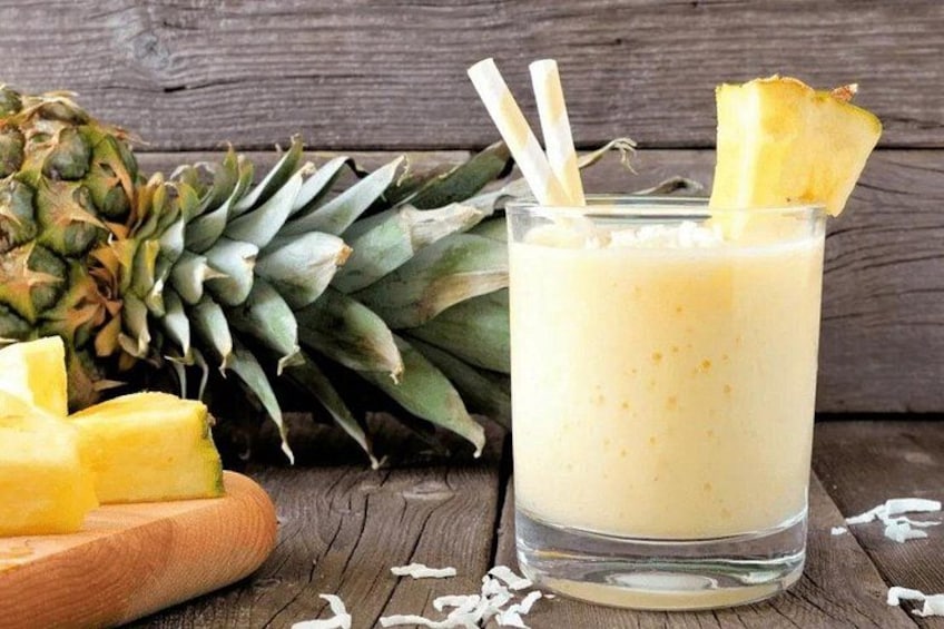Ein Glas Ananassaft mit einer Ananas Scheibe, eine ganze Ananas und ein Schneidebrett mit Ananasstücken. 4