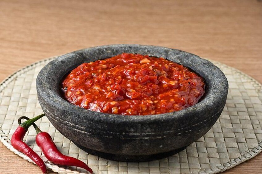 Eine Schüssel rote Soße mit zwei roten Chilischoten daneben. 3
