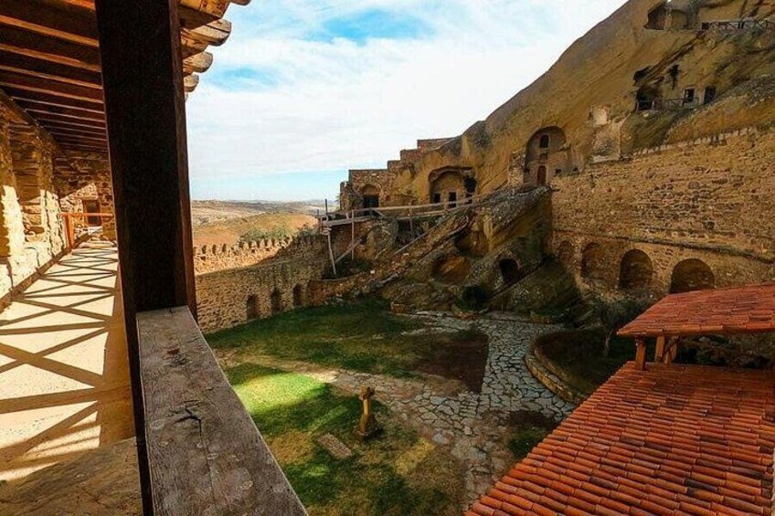Un cortile con mura in pietra, un ponte di legno e un tetto in tegole. 1