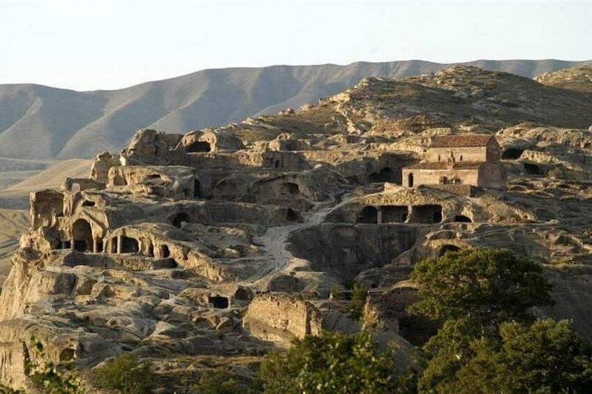 Architettura rupestre antica con numerose abitazioni scavate nella roccia e un piccolo edificio su un pendio. 2