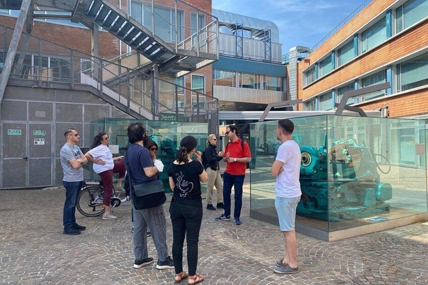 Un groupe de personnes se tient devant une enceinte en verre, à l’intérieur de laquelle se trouve une pièce mécanique. 1