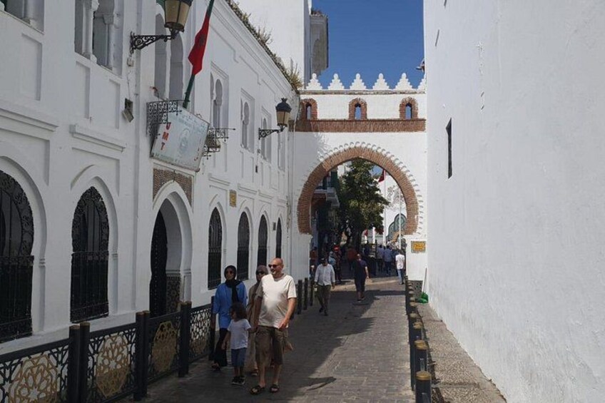 A narrow street with white buildings, an arched gateway, and pedestrians. 2