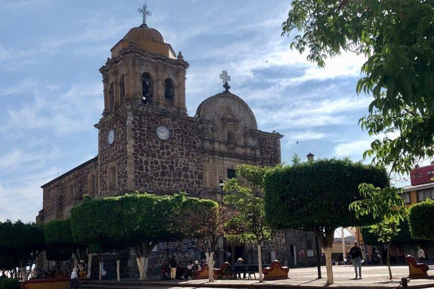 A historic church with a bell tower and dome, surrounded by a plaza with benches and trees. 3