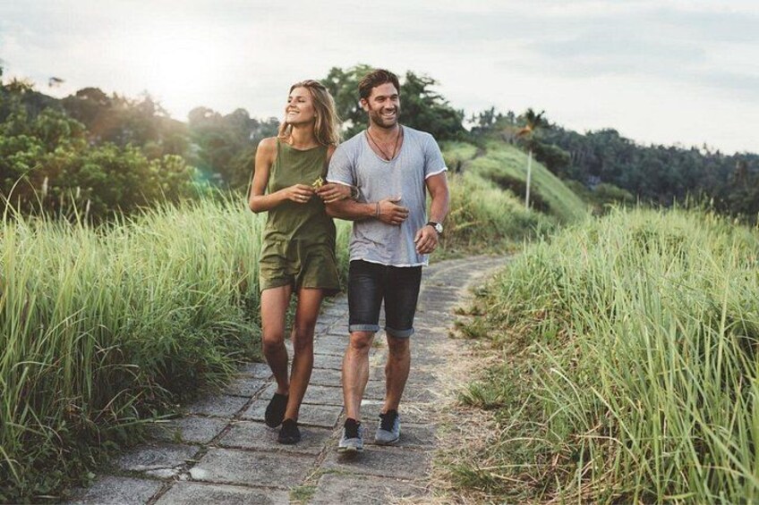 A couple walking on a stone path surrounded by tall grass and trees. 2