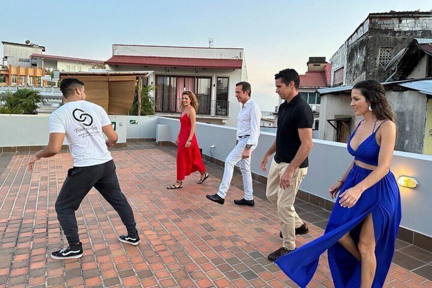 A group of people on a rooftop with a brick floor, buildings in the background, and a clear sky. 1