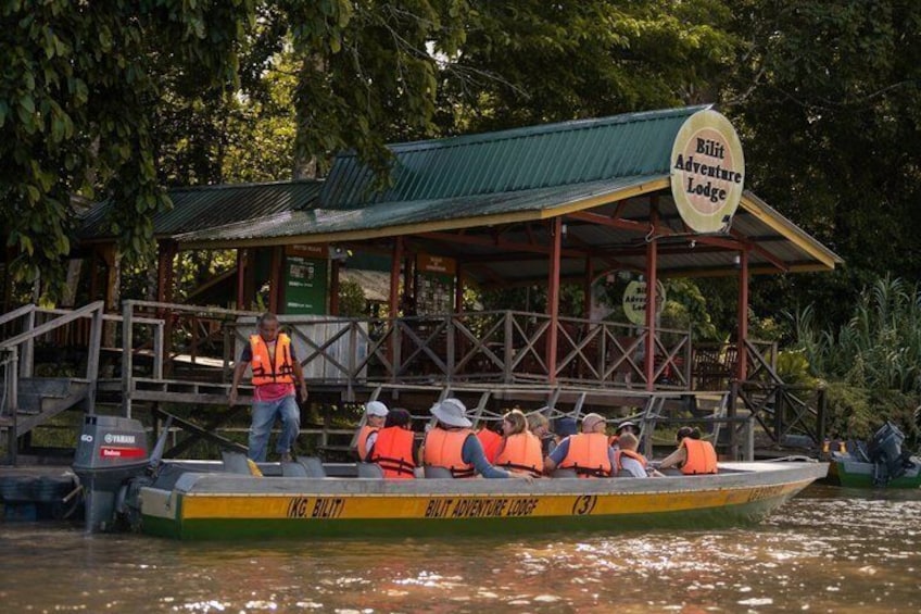 A boat with people wearing life jackets, a dock, and a sign for Bilfit Adventure Lodge. 1